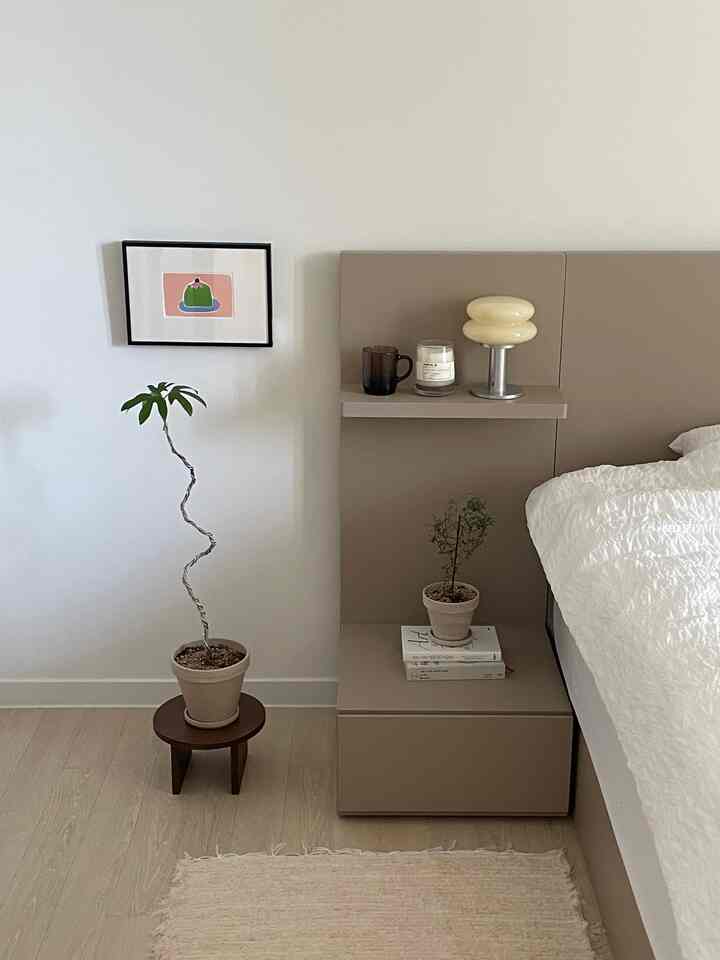 ベージュとホワイトの色調の寝室、ナチュラルモダンなベッドとナイトテーブル、小さな植物と額縁のある印象的な空間