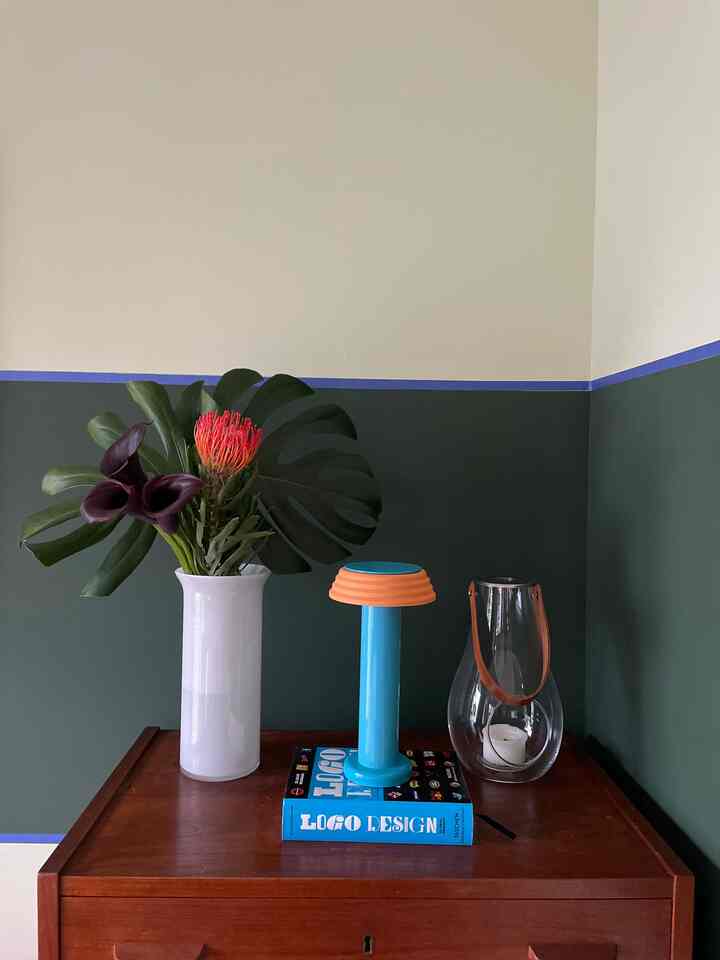 Stylish corner display with dark green walls and wooden console table featuring pink flowers in white vase and a blue table lamp