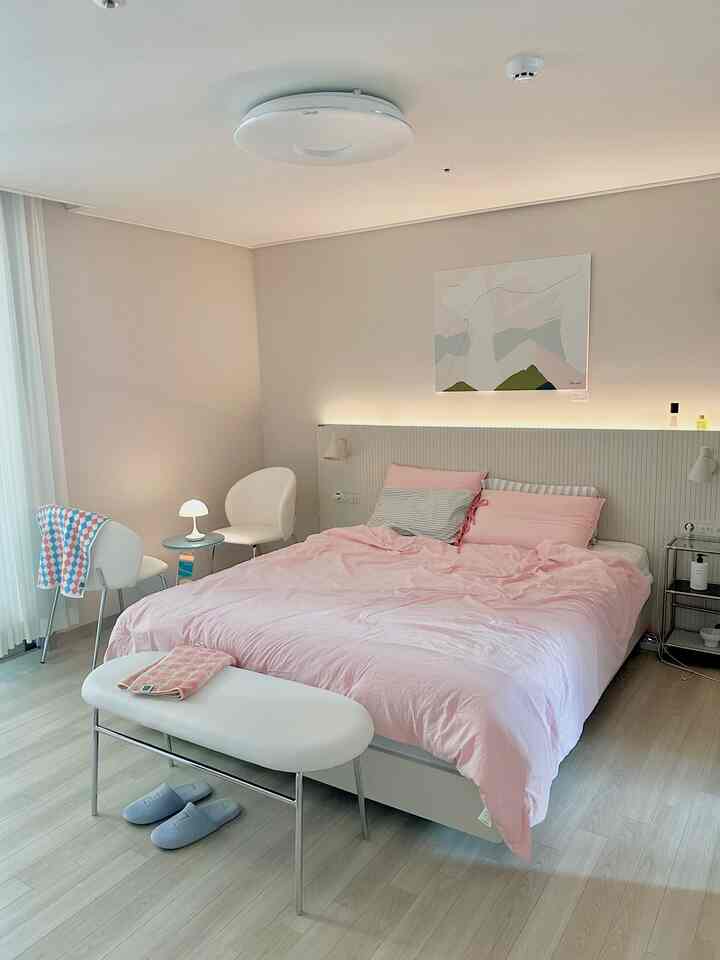 ホワイトとパステルピンクのトーンの寝室、ピンクの寝具とホワイト家具が配置され、落ち着いた清潔感のあるインテリア空間