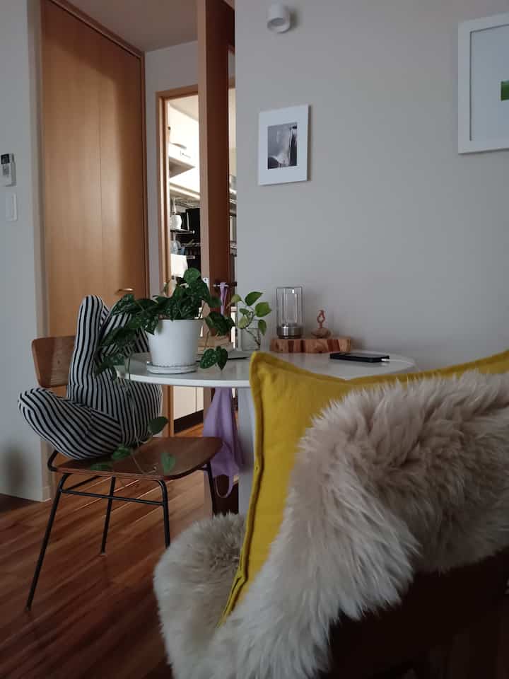 Natural-toned dining room featuring a white round table, yellow cushion, and green plants creating a cozy atmosphere