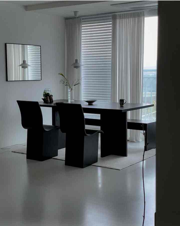 Modern dining room in white and black tones with large windows and curtains allowing natural light
