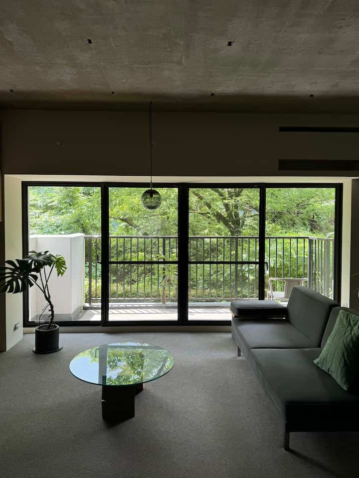 A modern living room with gray carpet and furniture, featuring a balcony view and a bright natural atmosphere