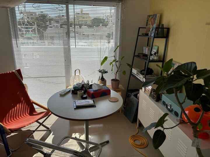 白とオレンジのトーンの小さなリビング、丸テーブルとオレンジの椅子、多数の植物が配置された雰囲気のある空間