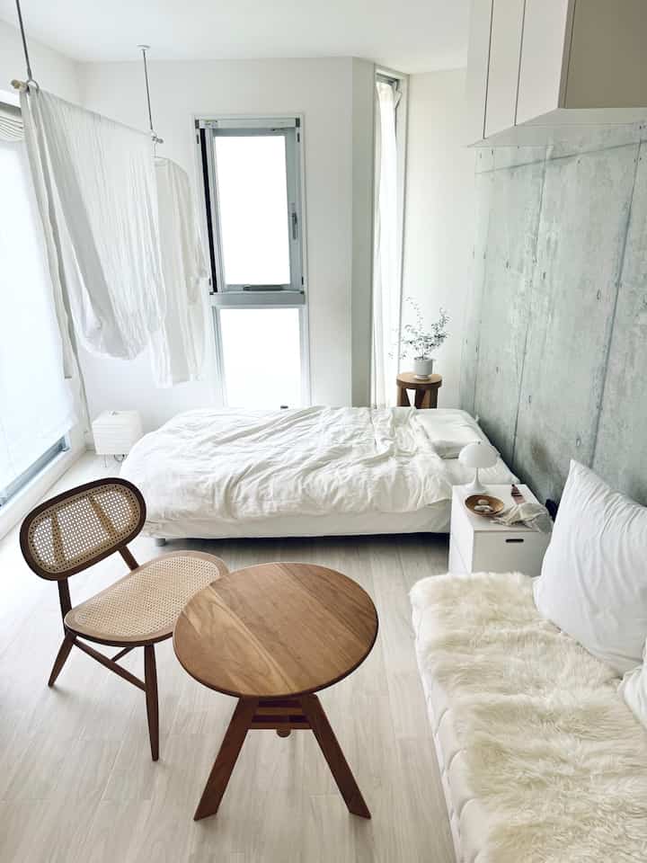 白とウッドトーンの小さな寝室、自然素材の家具とシンプルなレイアウトが印象的な空間
