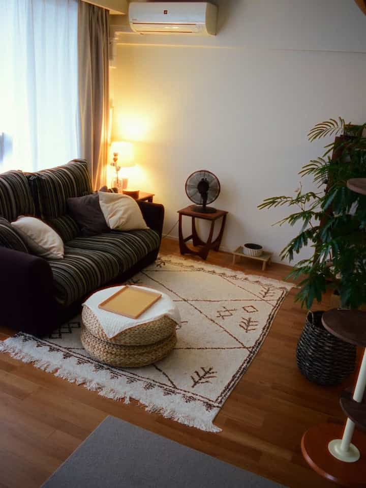 Warm wood tone flooring and vintage style sofa in cozy living room featuring leafy plants, a cat tower, round stool, and patterned rug