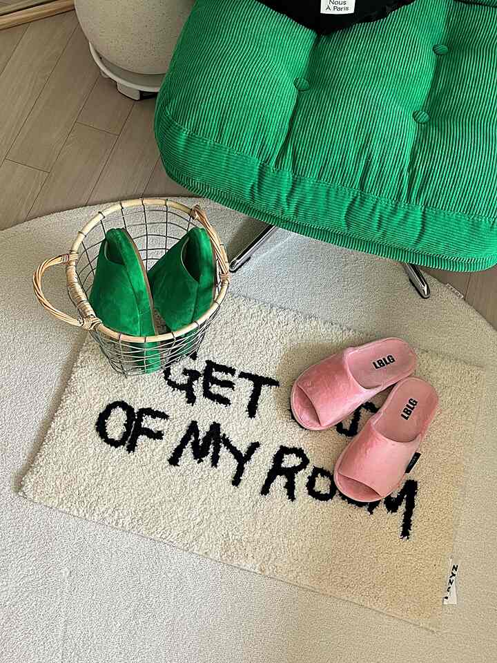 Cozy room with wood tone flooring, green armchair, pink slippers on a neat white rug with black text