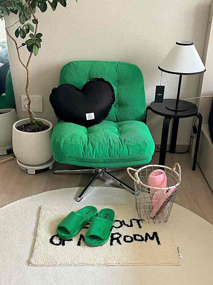Cozy bedroom corner featuring a green armchair and rug with a black heart cushion and lamp