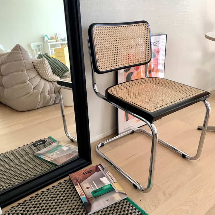 ナチュラルな木目調の床と黒いフレームの鏡、ラタン椅子が配置された自然な印象の玄関スペース