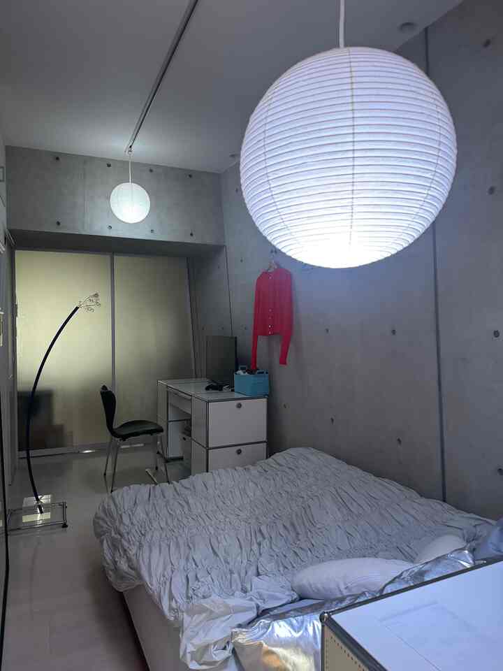 グレーとホワイトのトーンの寝室、大型ペンダントライトとミニマルな家具が配置されたシンプルな空間