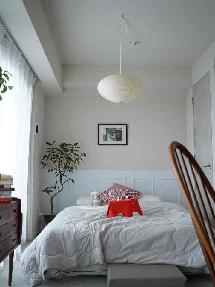 白とナチュラルカラーの寝室、白い寝具の中央に赤いゾウのスツールが置かれた清潔感のあるインテリア