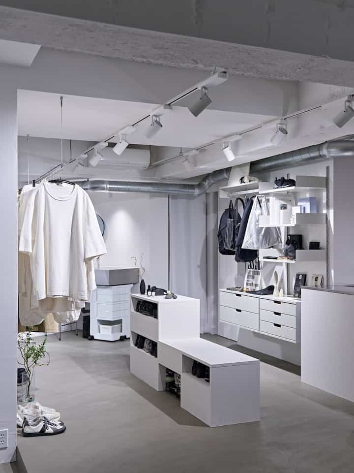 白を基調とした横長でコンパクトなワンルーム、モダンな収納家具と靴が整頓されたベンチが配されたミニマルなインテリア