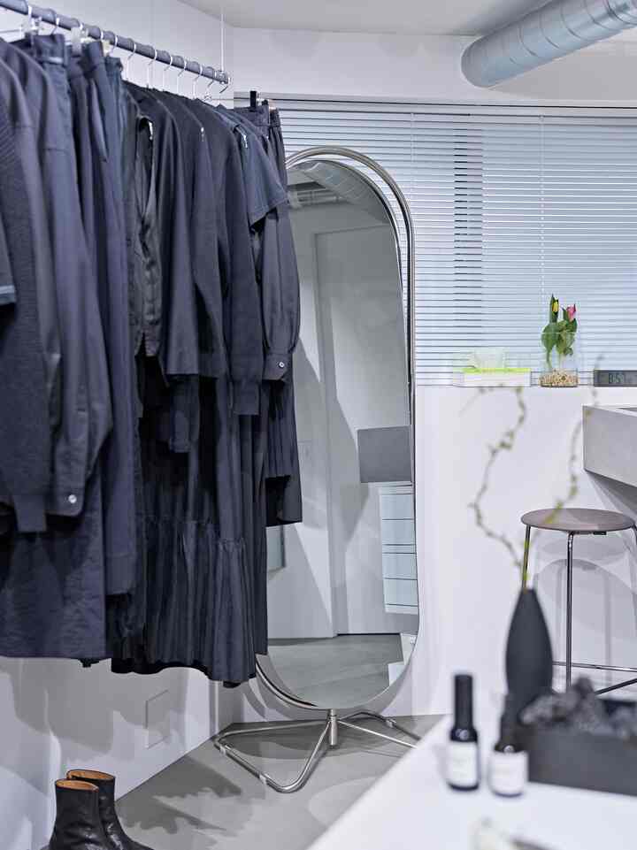 白色調の狭いモダンな部屋、シルバースチールの鏡と黒い服がかかったワードローブがある清潔な空間