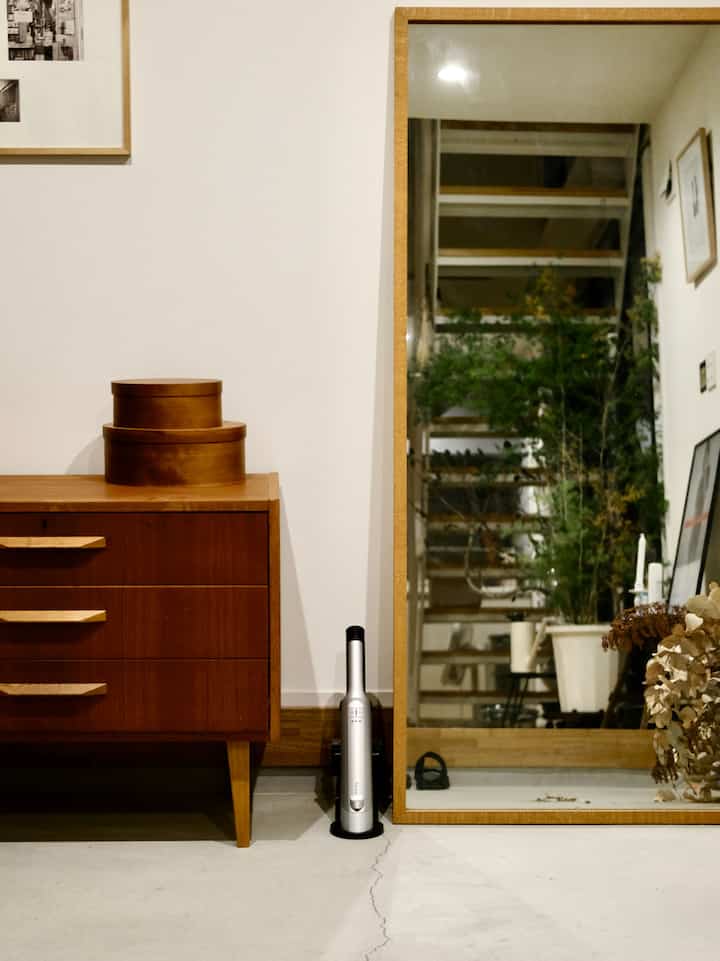 Minimal entrance space with white walls and floor, wood-tone dresser and large mirror