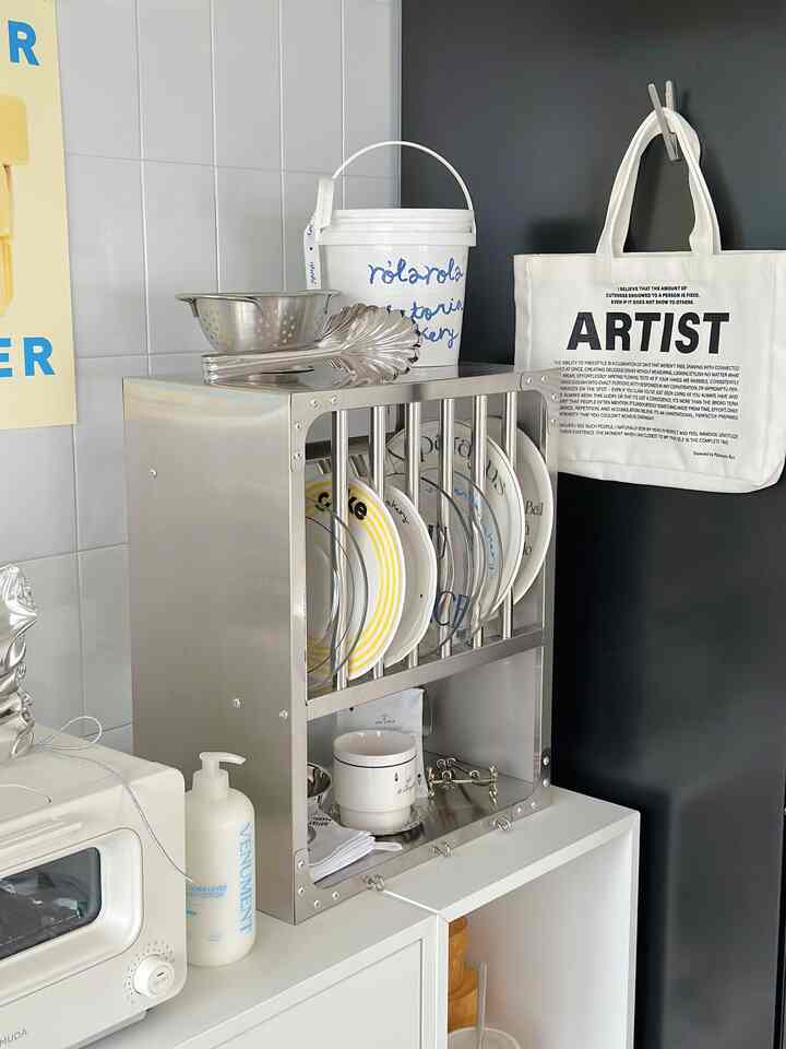Silver and white toned kitchen space featuring a stainless kitchen rack with neatly arranged plates and cooking utensils