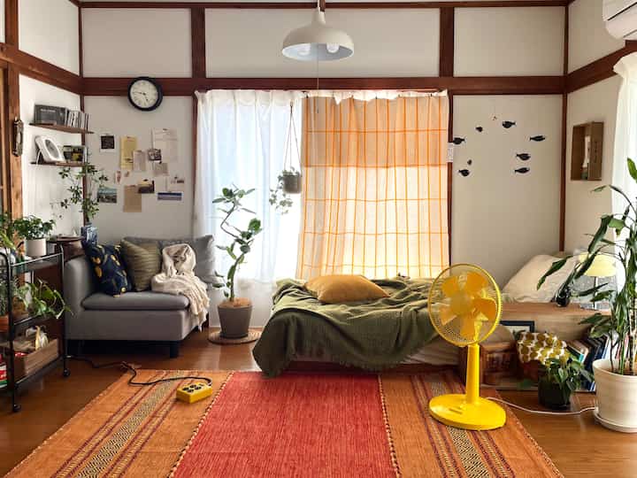 オレンジと黄色の色調が調和したナチュラルな一人暮らしのリビング、ベッドとソファが配置された落ち着いた空間