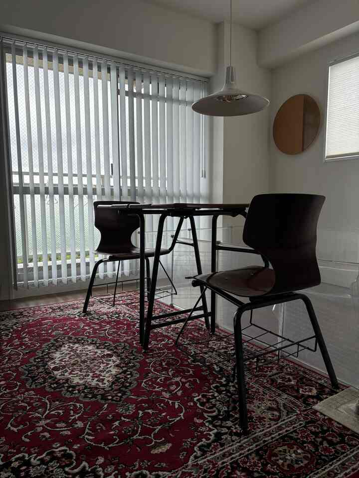 白い縦型ブラインドが印象的な明るいダイニング、赤い柄のラグと木目調のミッドセンチュリーモダンのダイニングテーブルが配置された空間