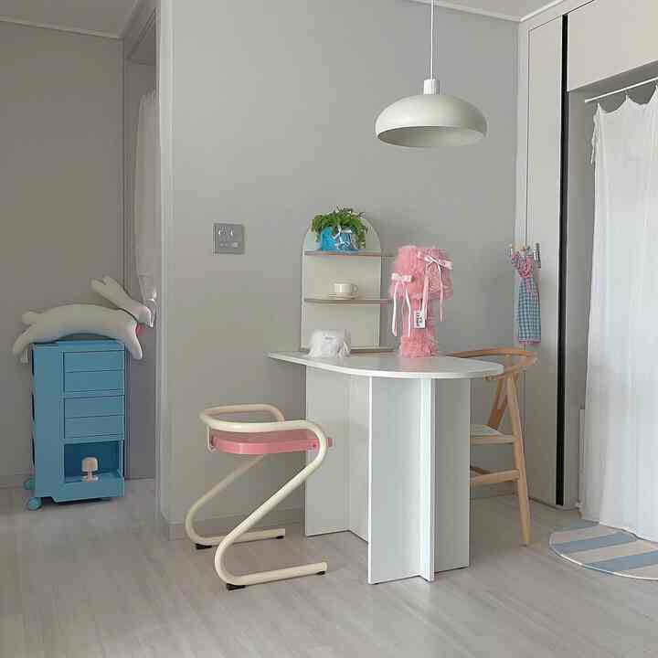 Studio apartment dining area in white and wood tones with mid-century modern chairs and a central pendant light, showing a clean, natural interior