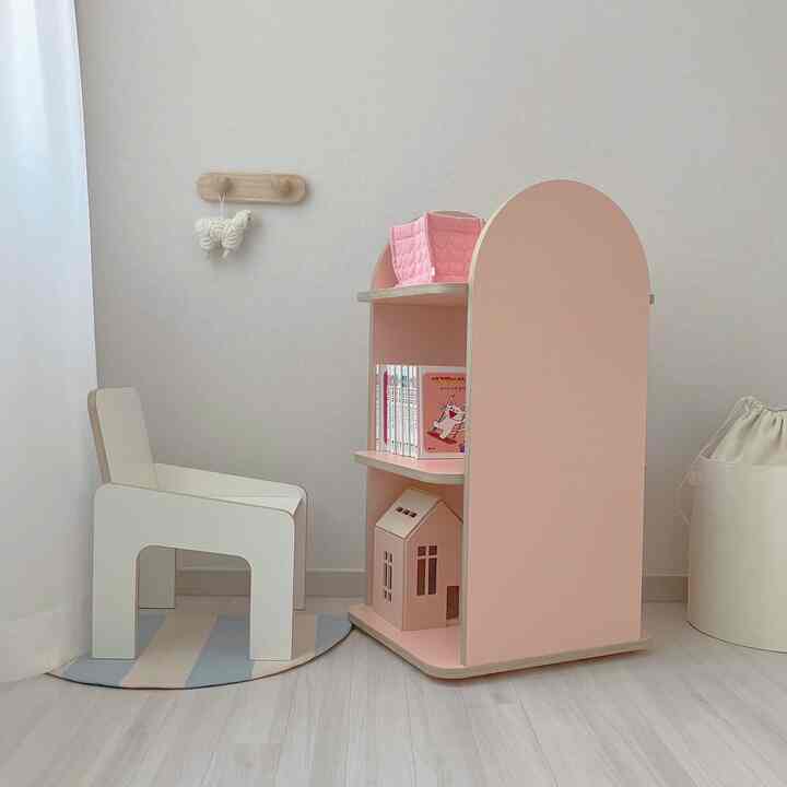 Beige and pink toned kids' room featuring a small chair and pink bookshelf with children's items, cozy and neat space