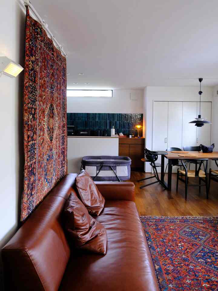 Natural modern living room and kitchen with brown leather sofa, wood tone flooring, and a colorful carpet