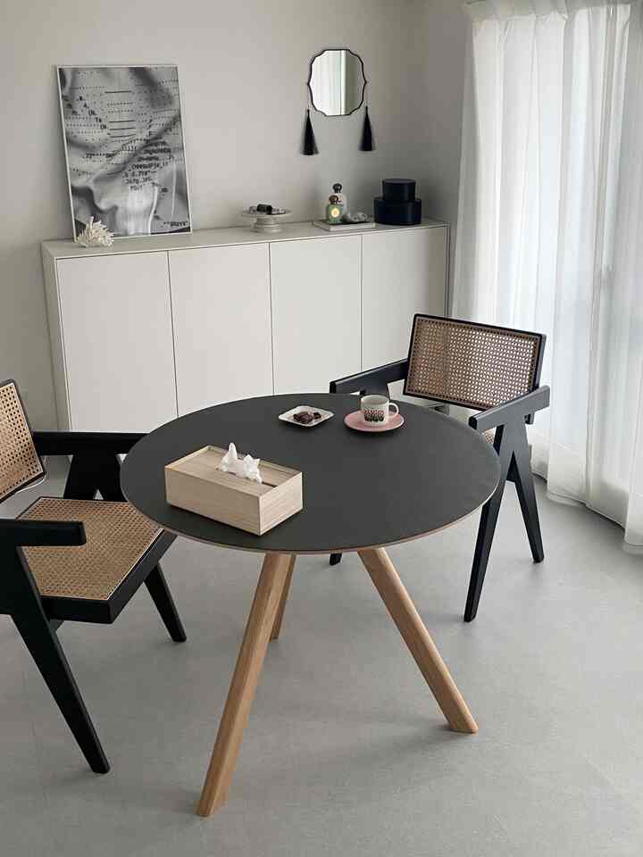 Modern dining room with black round table top and wood tone legs, white cabinet and curtains creating a bright and clean atmosphere