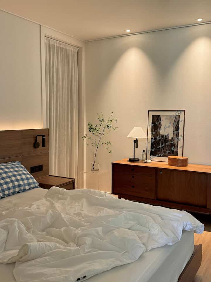 Beige and white toned bedroom featuring wood dresser and hotel bed with white bedding creating a cozy atmosphere