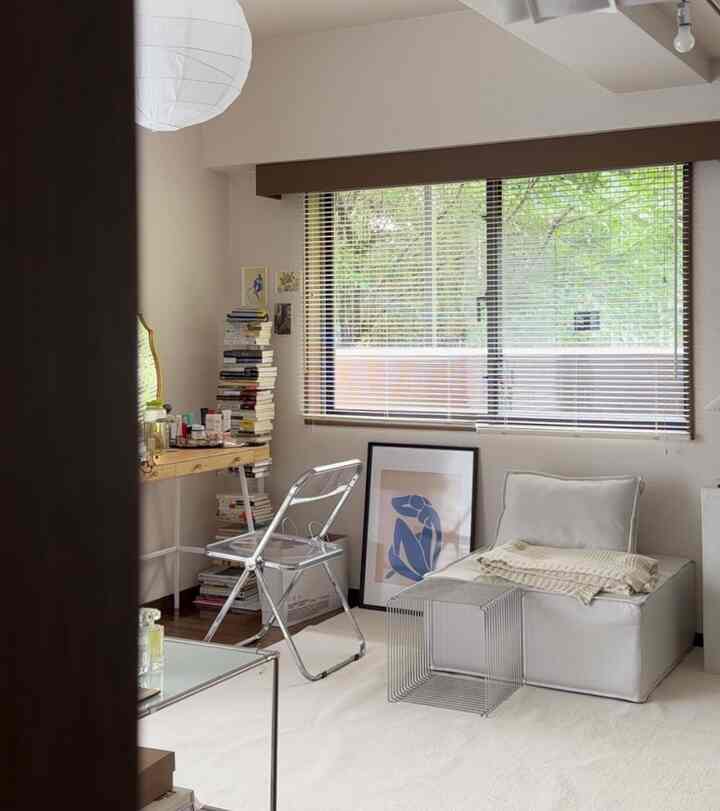 ナチュラルな色調の小さなリビングルーム、モダンな折りたたみ椅子とコンパクトなソファ、デスクが配置されたシンプルで落ち着いた雰囲気のインテリア