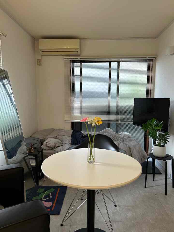 White and gray toned studio apartment featuring a round cafe table with flowers in a simple single household space