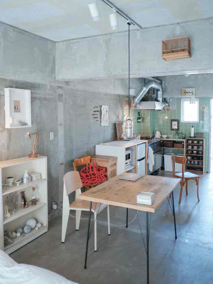 A compact single household kitchen and dining area featuring natural wood furniture against cool gray concrete walls