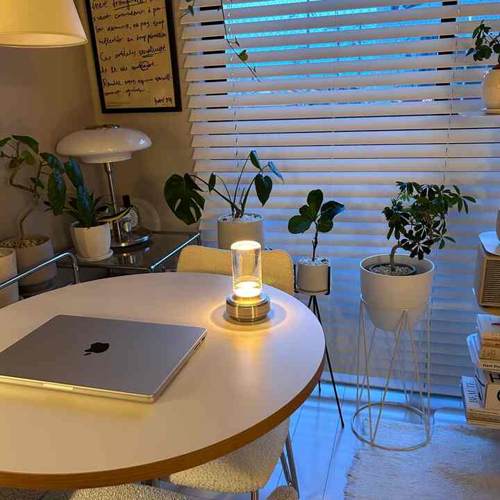 白と木目調のモダンなホームオフィス、円形ダイニングテーブルとテーブルランプ、多数の植物が配置された自然でミニマルなインテリア