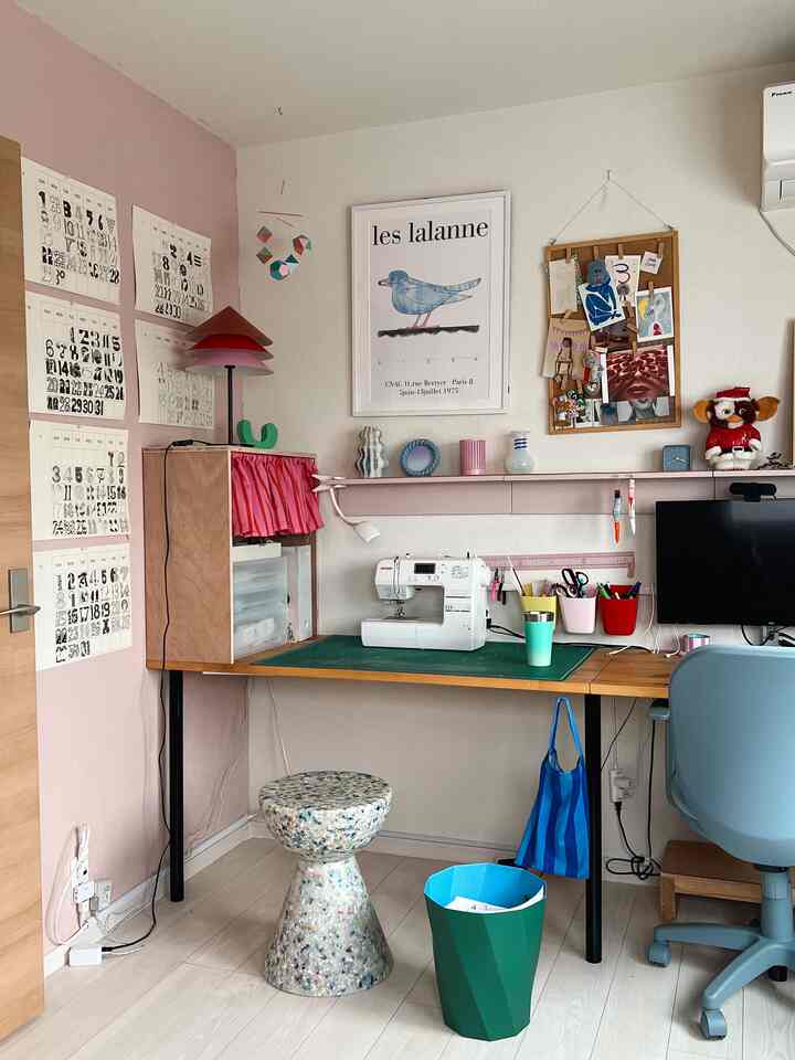 A cozy home office space in pink and white tones featuring a sewing machine, desk, and a blue office chair