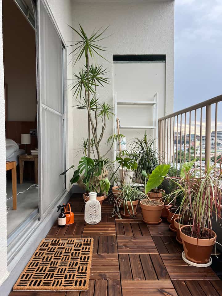ナチュラルな木目調の床に多様な鉢植えが置かれた陽光あふれるバルコニーのインテリア