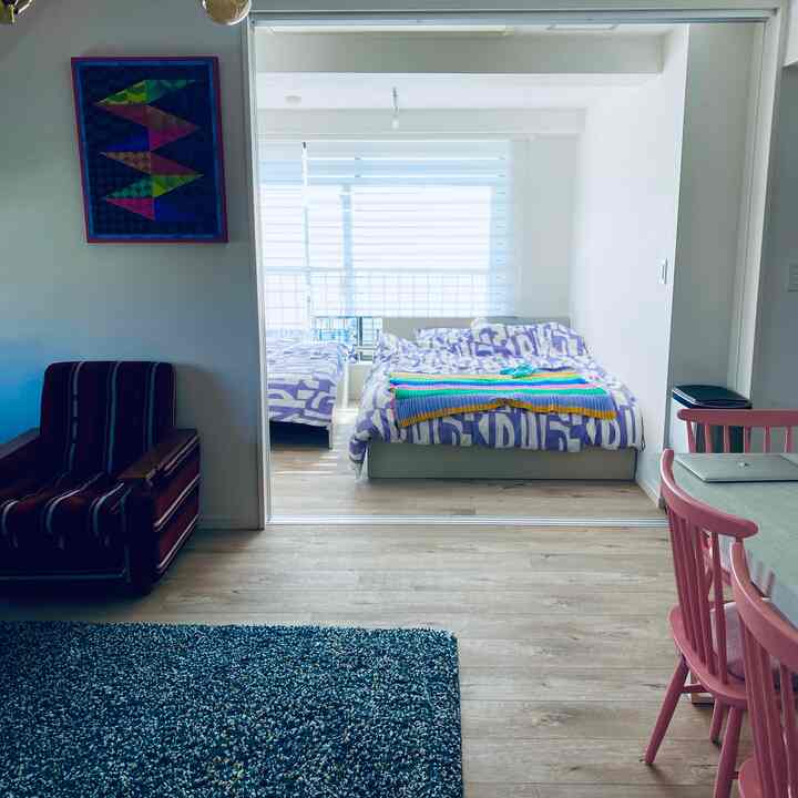 Natural-toned studio apartment featuring beds, a sofa, and pink dining chairs in a cozy living and bedroom combined space