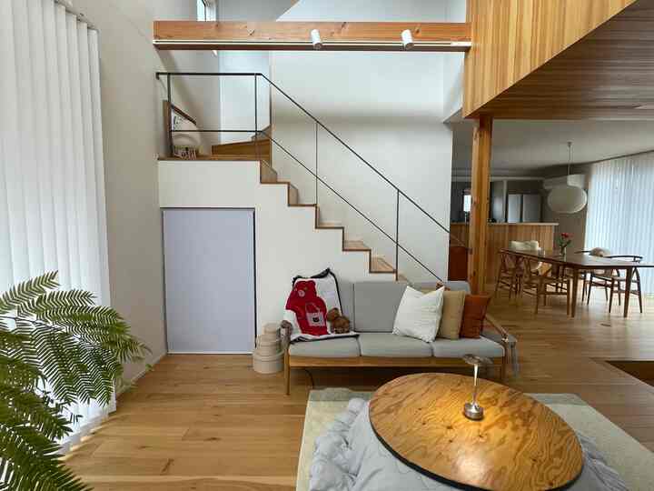 ナチュラルな色調のリビング、木製の階段横にグレーのソファとDIYこたつテーブルが配置された雰囲気あるインテリア