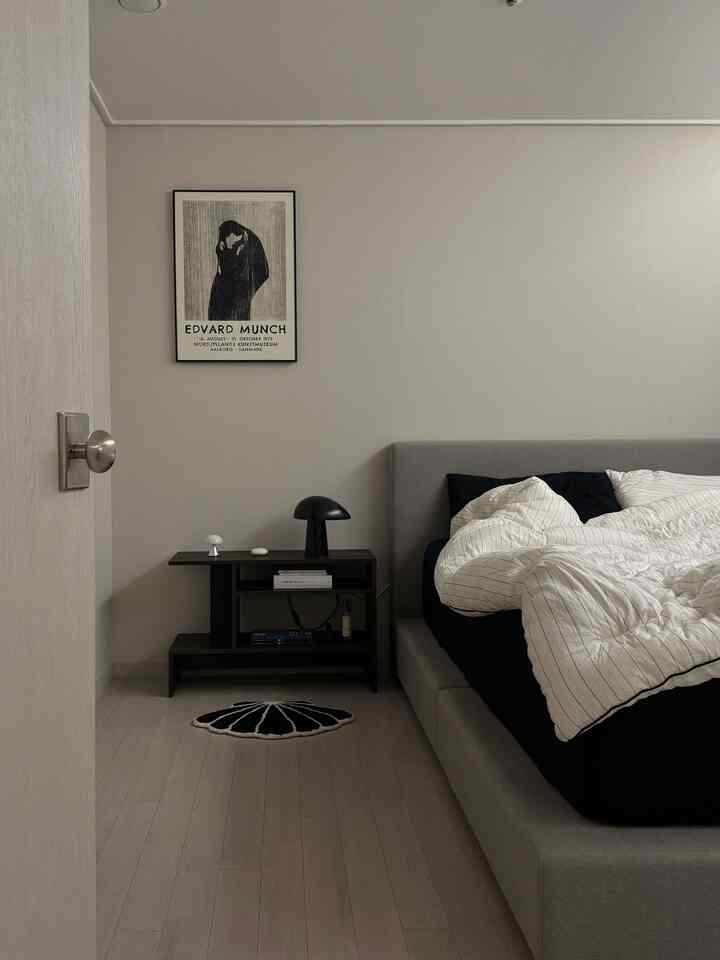 ライトグレーとブラックの色調の寝室、ベッドフレームとマットレス、サイドテーブル、額縁が調和したシンプルなインテリア