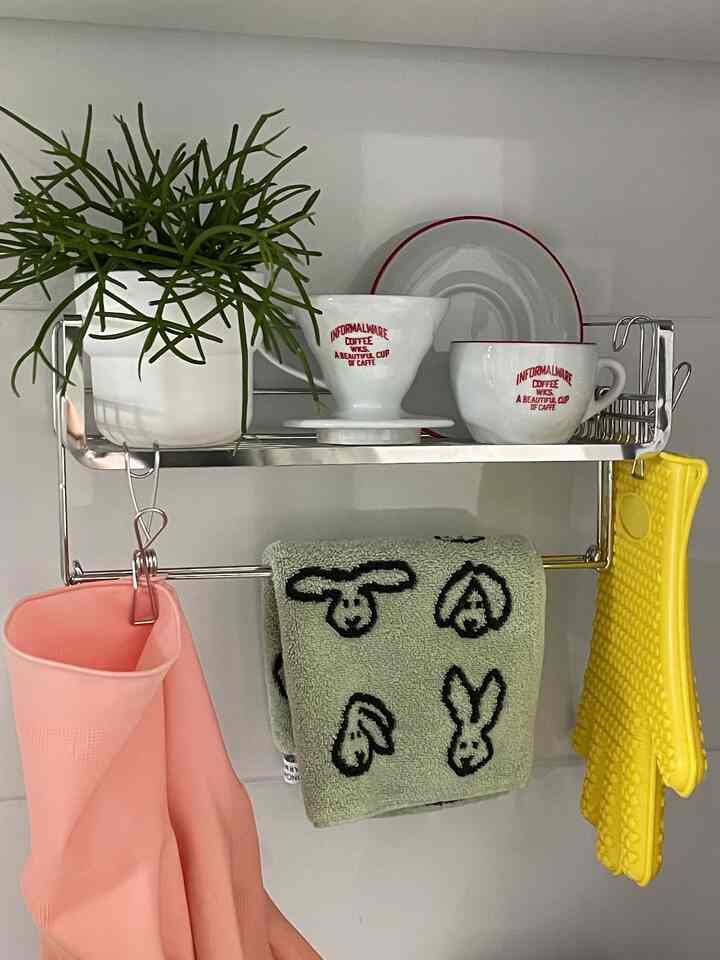 Metal kitchen shelf mounted on white wall with plant, cups, and colorful towels hanging, creating cozy kitchen accessories vibe