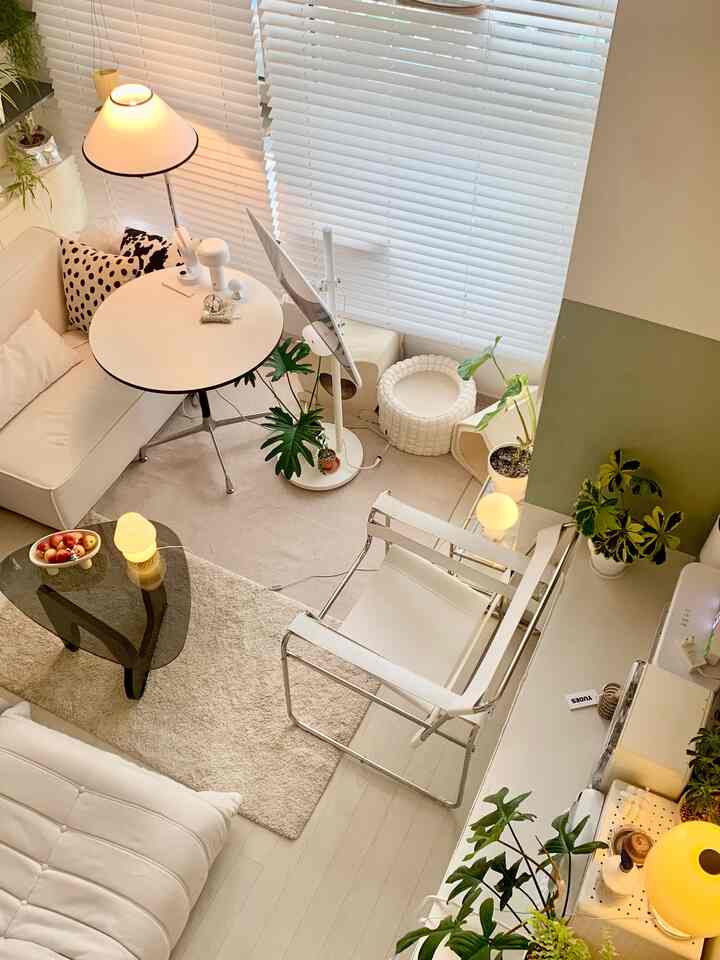 Bright white and beige toned studio living room featuring plants and floor lamps creating a cozy atmosphere