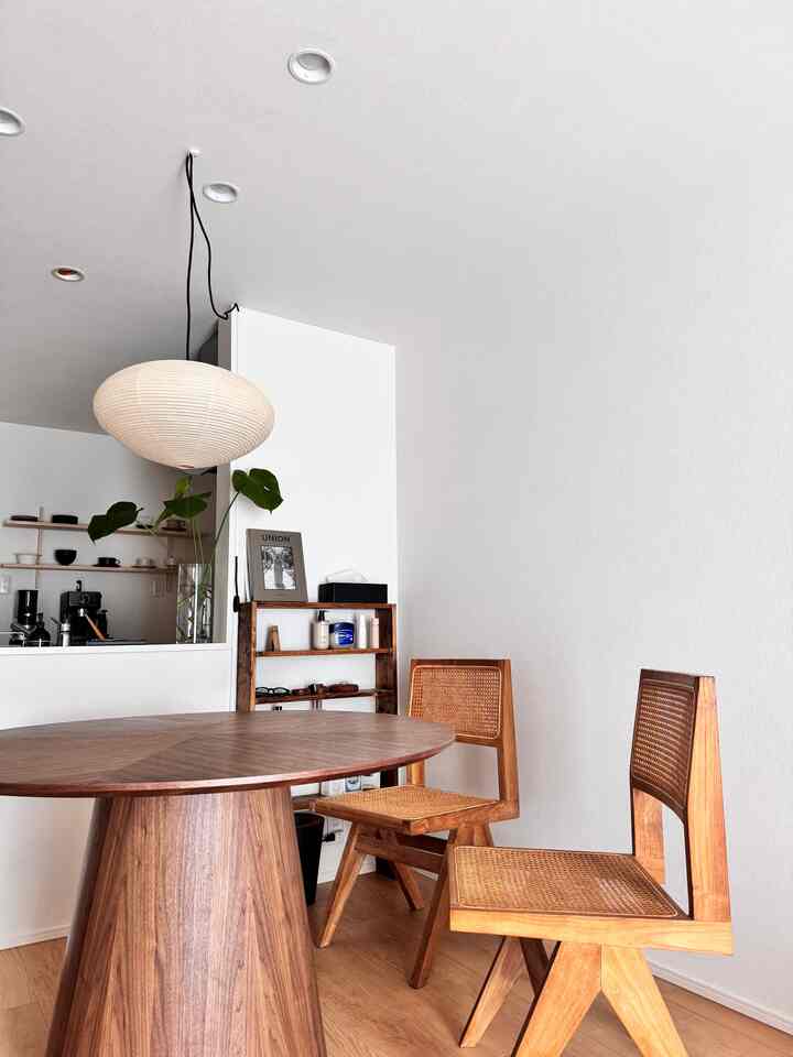 白い壁と木目調の丸いダイニングテーブル、木製の椅子二脚、丸いペンダントライトが配置されたモダンなダイニング