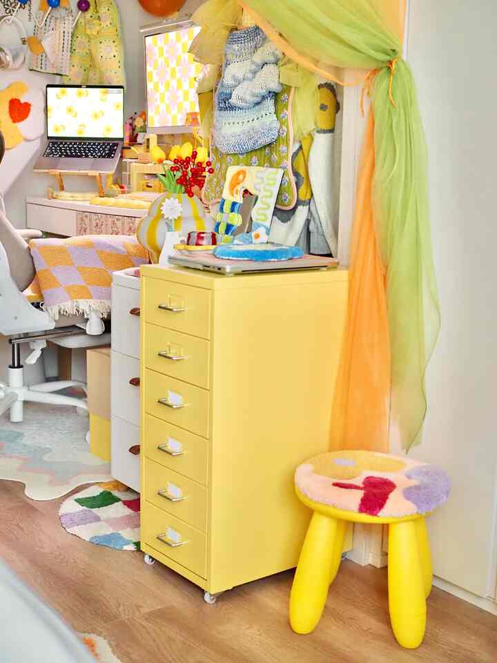 A cozy small room in dominant yellow tone featuring a yellow mobile drawer unit and a yellow stool within a study space