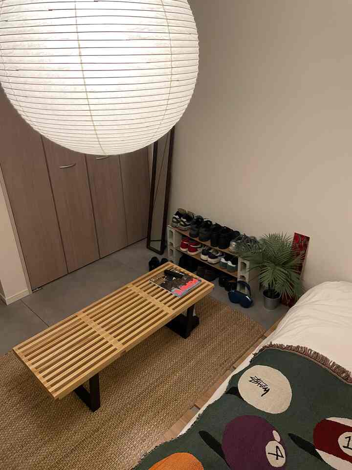 ライトブラウンの小さな寝室、中央に木製スラットのベンチとベージュのラグが配置されたシンプルで北欧風のインテリア