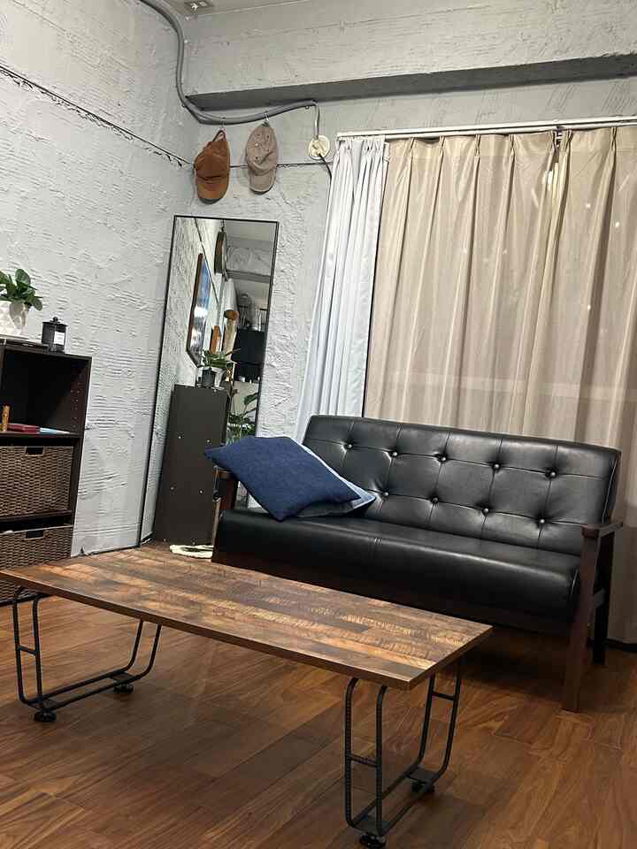 Natural modern living room with brown wood tone floor and coffee table, black leather sofa, and beige curtains