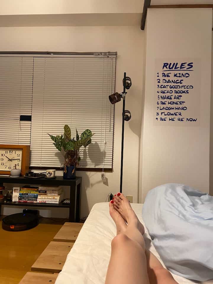 木目調の床とベッドフレームが特徴的なミッドセンチュリーモダンの一人暮らし寝室、ブラインドとフロアランプが配置された雰囲気のあるインテリア