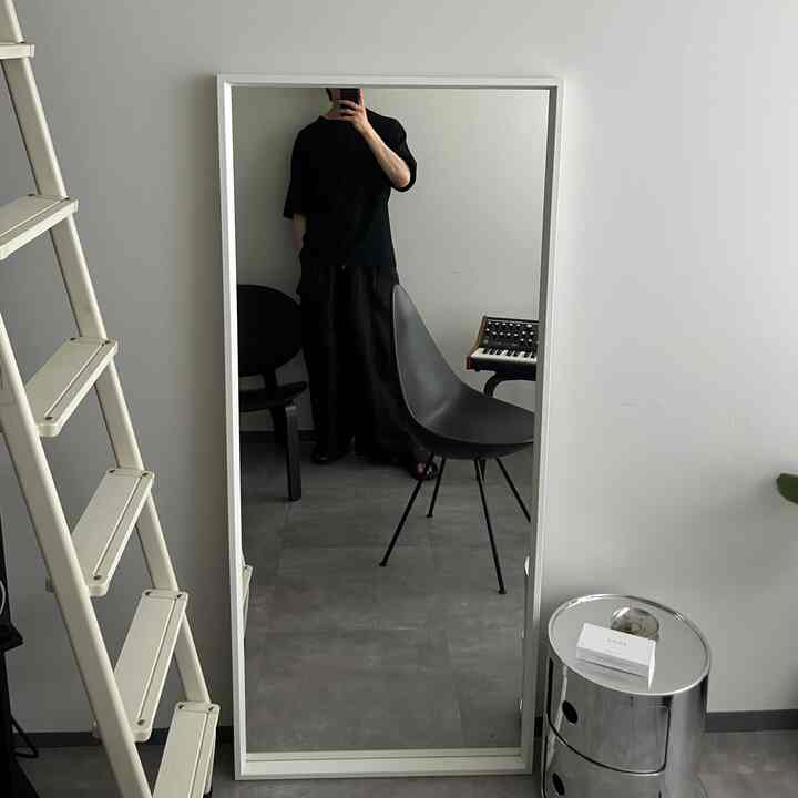 Modern narrow living room in white and gray tones featuring a large white-framed mirror and black chairs