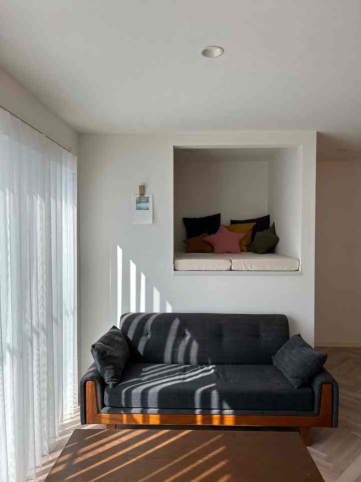 白と木目調の調和が取れたリビング、ダークグレーのソファと居心地の良いヌックスペースが配置された落ち着いた雰囲気のインテリア