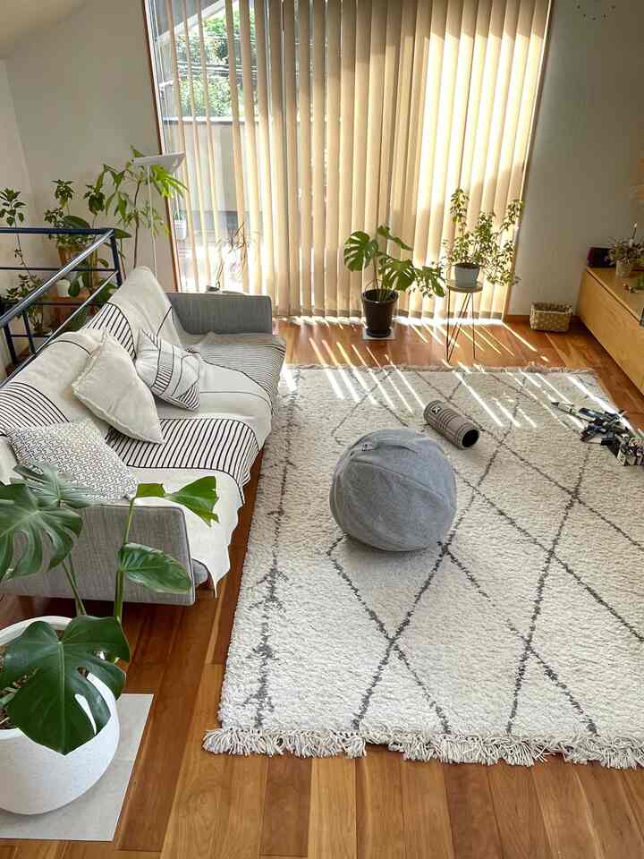 ナチュラルな色調のリビング、広いソファとラグ、多数の植物が配置された明るく居心地の良い空間