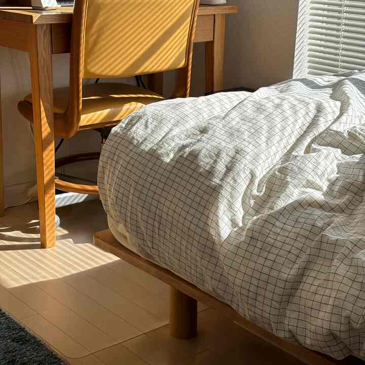 ナチュラルな色調の寝室、木製ベッドフレームと格子柄の掛け布団カバーが配置された雰囲気のあるインテリア