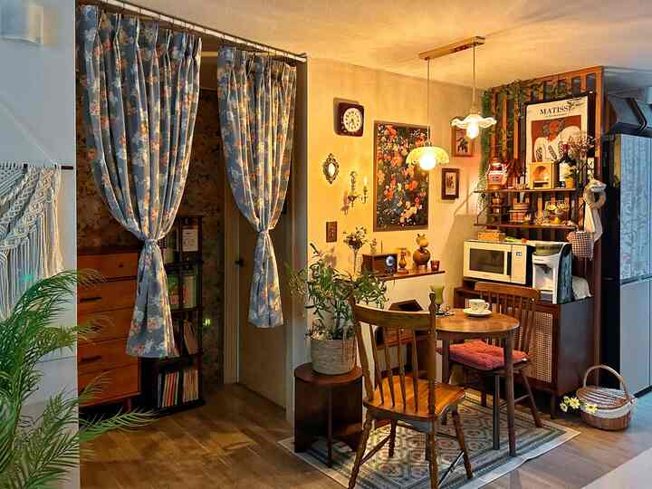 温かみのある照明と木製家具が調和したヴィンテージ風キッチン、花柄のカーテンとヴィンテージ雑貨が配置された雰囲気のある空間