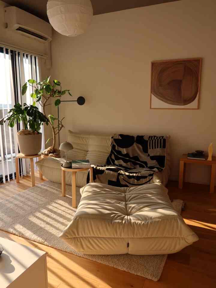 Warm natural-toned living room featuring cream modular sofa, green plants, and simple wooden stools with cozy atmosphere