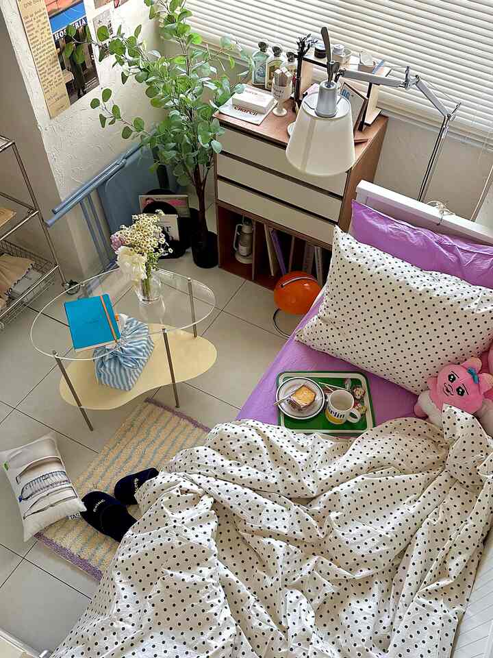 白と紫のトーンの寝室、水玉模様の寝具と植物が配置された雰囲気のある夏の寝室