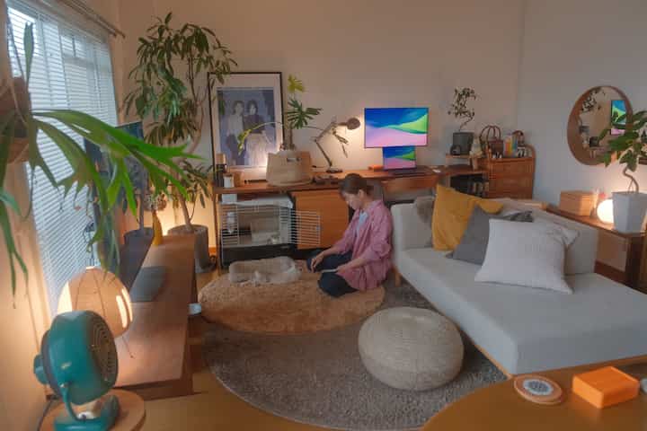 Cozy living room in warm natural tones featuring sofa, plants, rugs, and a home office setup