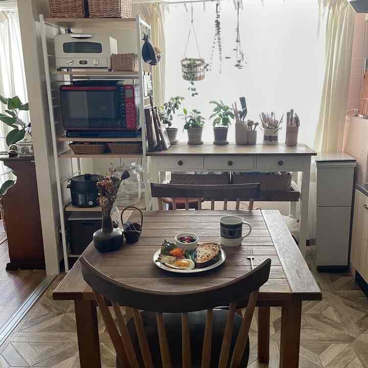 ナチュラルな木目調と白を基調としたキッチン、窓際のダイニングテーブルと椅子に植物や調理器具が配置された雰囲気のあるインテリア